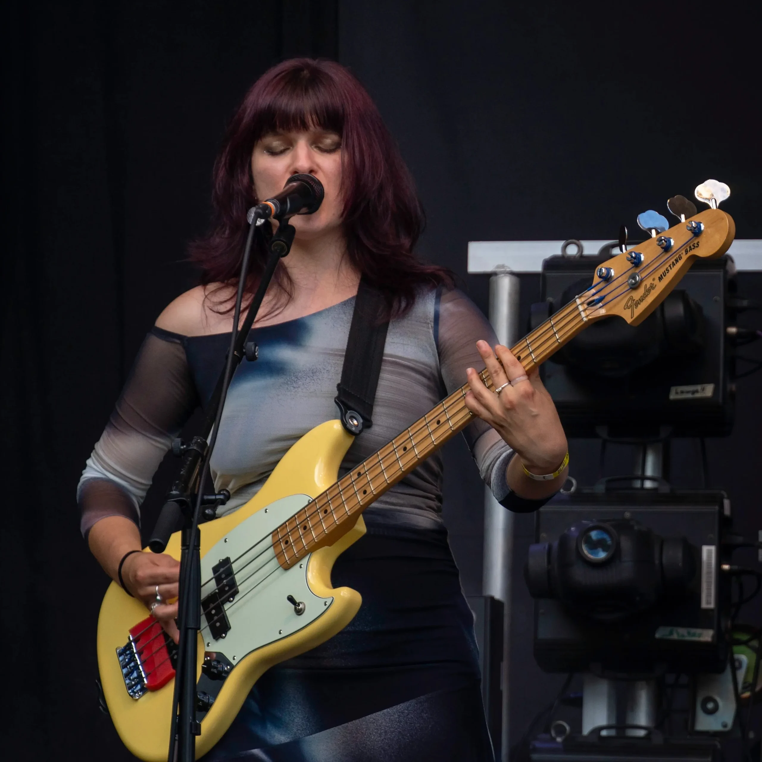 Musikerin spielt E-Bass und singt auf einer Bühne.