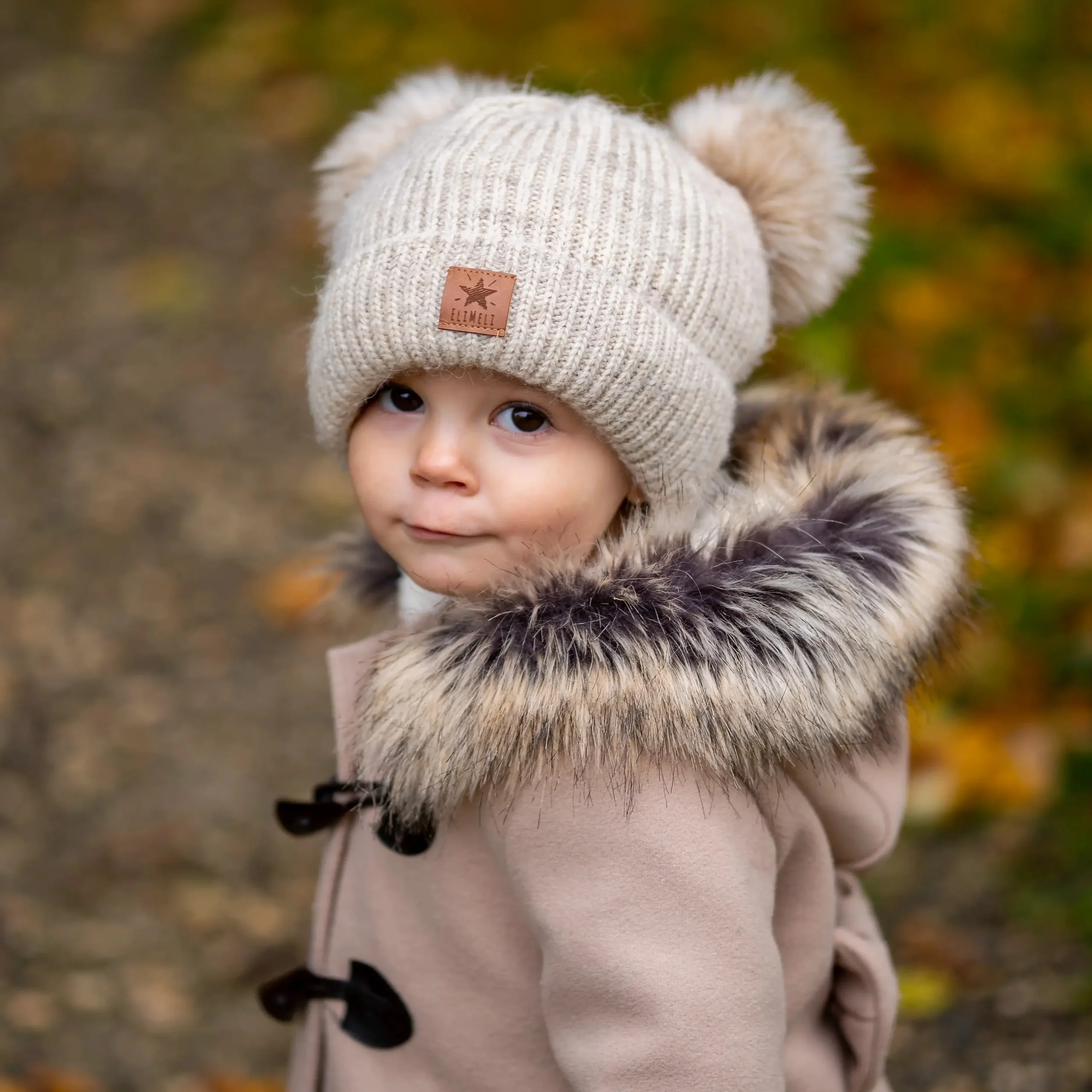 Kind mit beiger Mütze und Felljacke blickt in die Kamera, im herbstlichen Park.