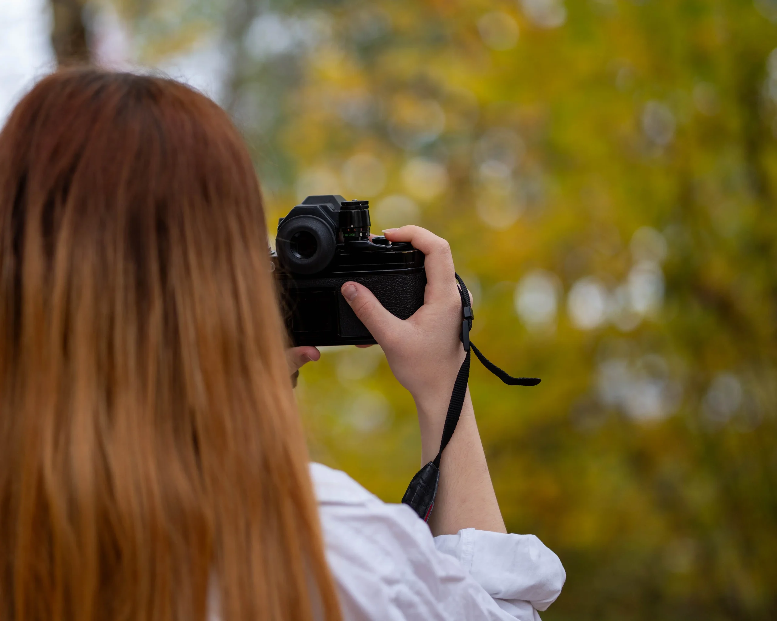 Person mit langen Haaren fotografiert mit einer Kamera im herbstlichen Wald.