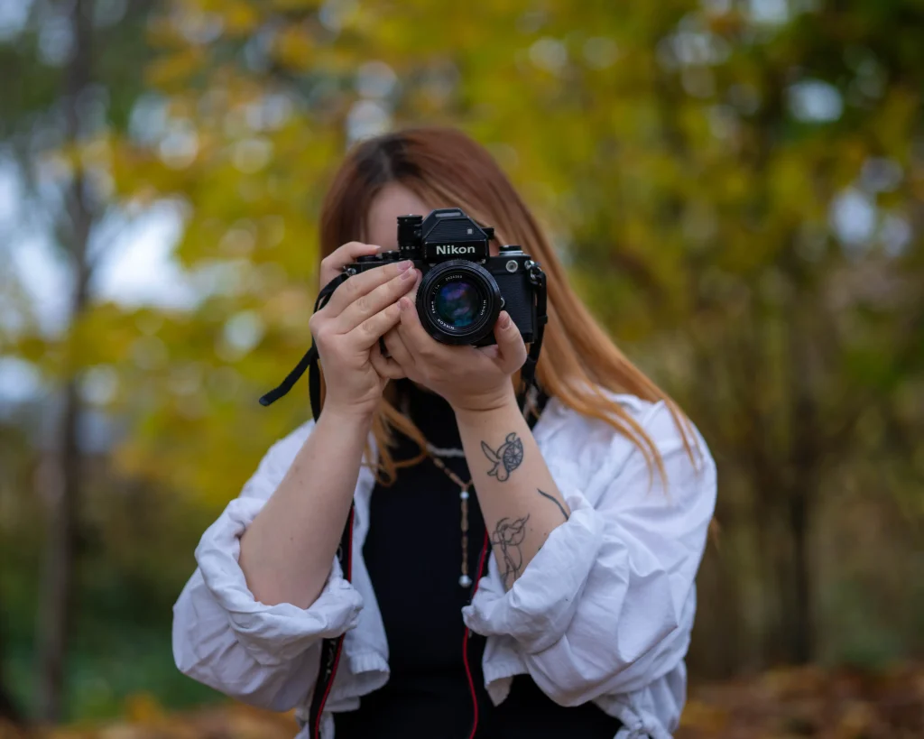 Person hält eine Nikon-Kamera und fotografiert im herbstlichen Park.